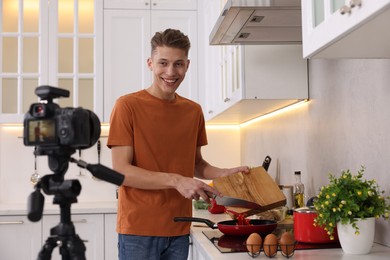 Photo of Smiling food blogger cooking while recording video in kitchen