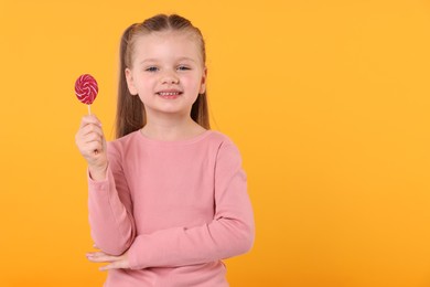 Happy little girl with bright lollipop swirl on orange background, space for text