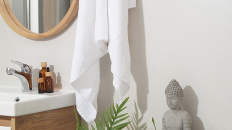 Photo of Hanging towel, sink, toiletries and houseplant in bathroom. Interior design
