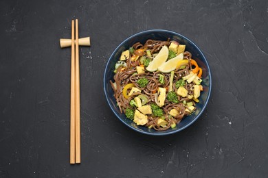 Photo of Stir-fry. Delicious cooked noodles with chicken and vegetables in bowl served on gray textured table, flat lay