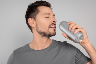 Photo of Happy man drinking from tin can on light grey background