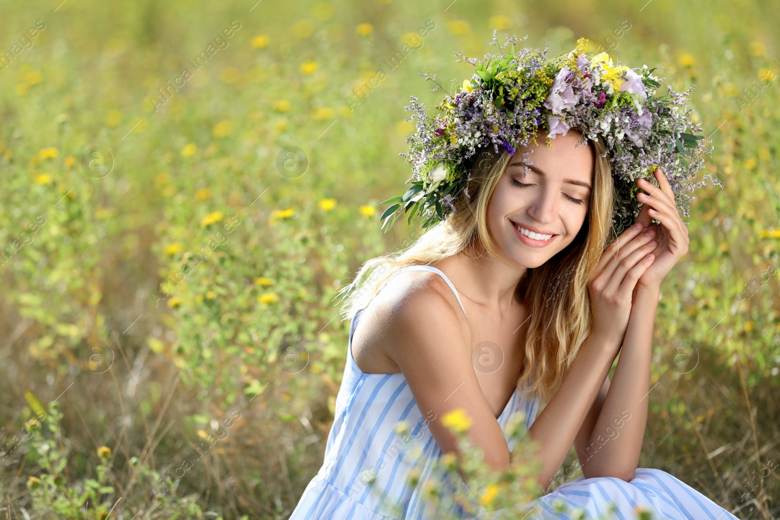 Photo of Young woman wearing wreath made of beautiful flowers in field on sunny day