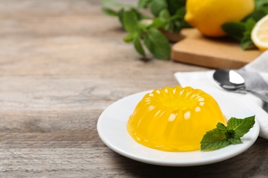 Photo of Delicious fresh yellow jelly with mint on wooden table. Space for text