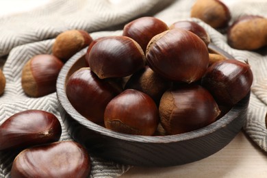 Photo of Sweet fresh edible chestnuts on light wooden table, closeup