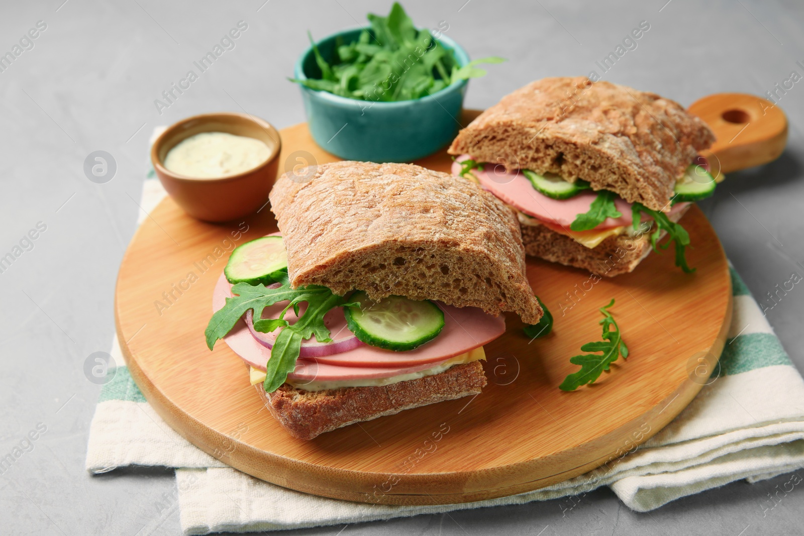 Photo of Tasty sandwiches with boiled sausage, cucumber, arugula and sauce on grey table, closeup