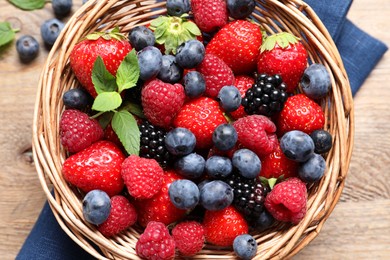 Many different fresh ripe berries in wicker basket on wooden table, top view