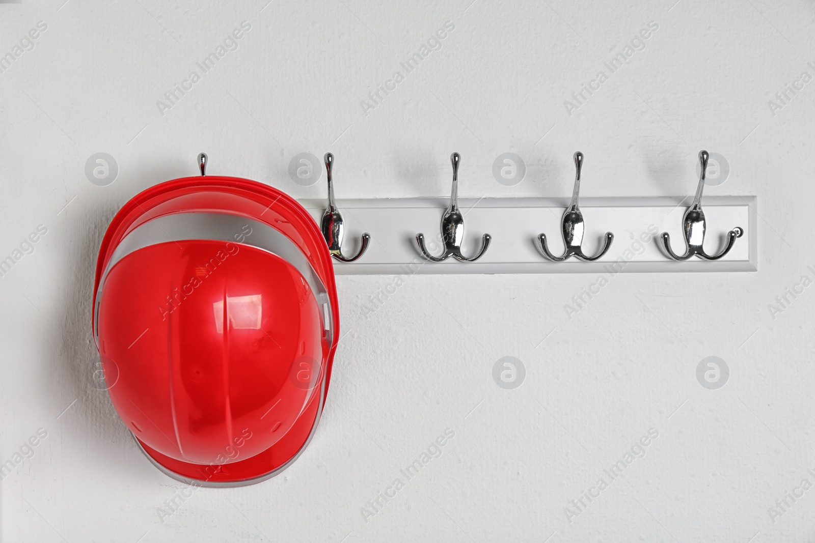 Photo of Hard hat hanging on white wall. Safety equipment