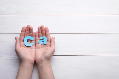 Photo of Woman holding paper symbol Ca (Calcium) at white wooden table, top view