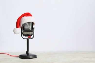 Photo of Retro microphone with Santa hat on wooden table against white background, space for text. Christmas music