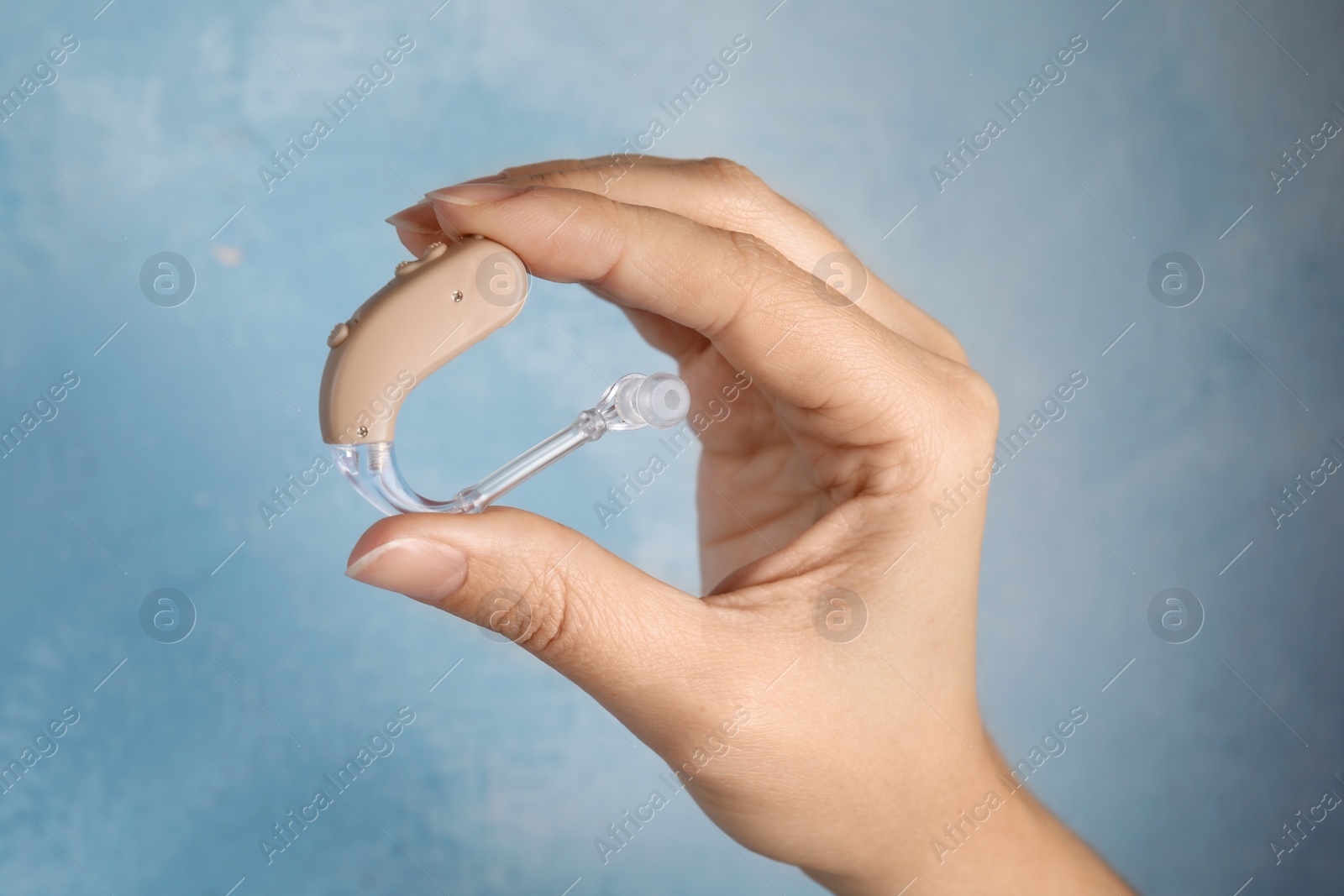 Photo of Woman holding hearing aid on color background, closeup