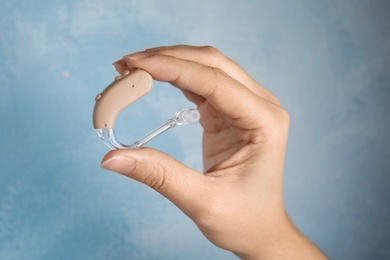 Photo of Woman holding hearing aid on color background, closeup