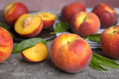 Photo of Fresh tasty peaches and leaves on grey table