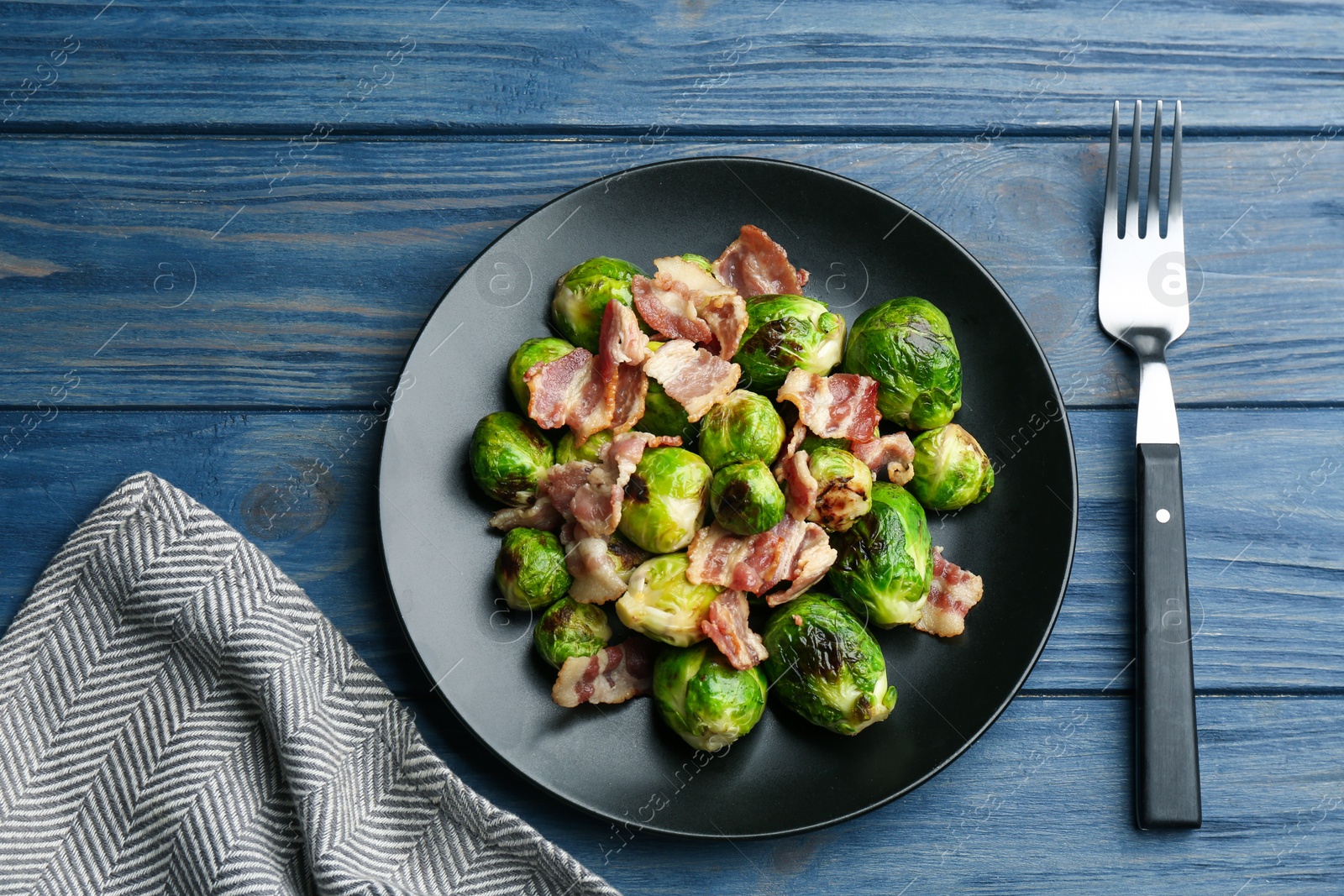 Photo of Delicious Brussels sprouts with bacon on blue wooden table, flat lay