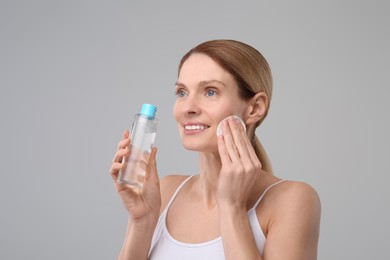 Photo of Beautiful woman removing makeup with cotton pad on gray background