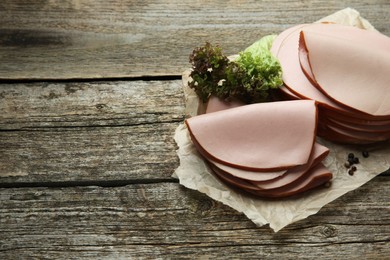 Photo of Slices of delicious boiled sausage with lettuce and spices on wooden table, space for text