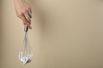 Photo of Woman holding whisk with whipped cream on beige background, closeup. Space for text