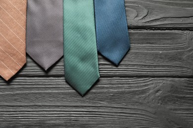 Photo of Different neckties on black wooden table, flat lay. Space for text