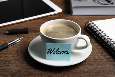 Image of Sticky note with word Welcome attached to cup of coffee on wooden office desk