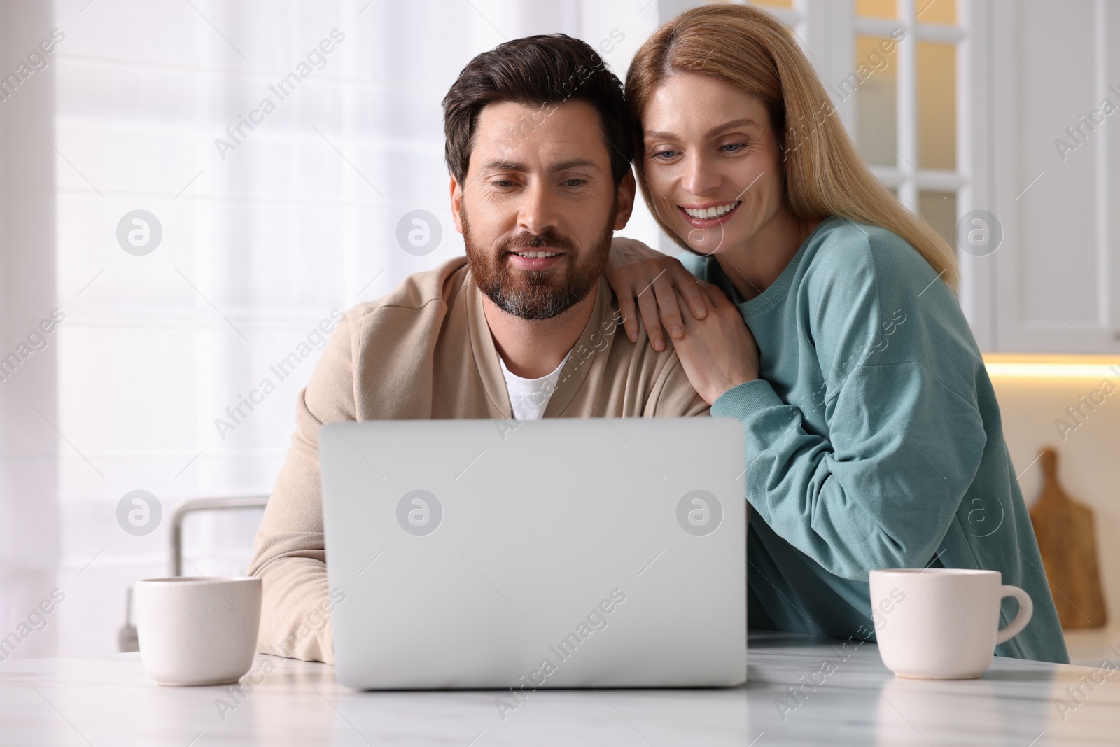 Photo of Happy couple with laptop at white table in kitchen