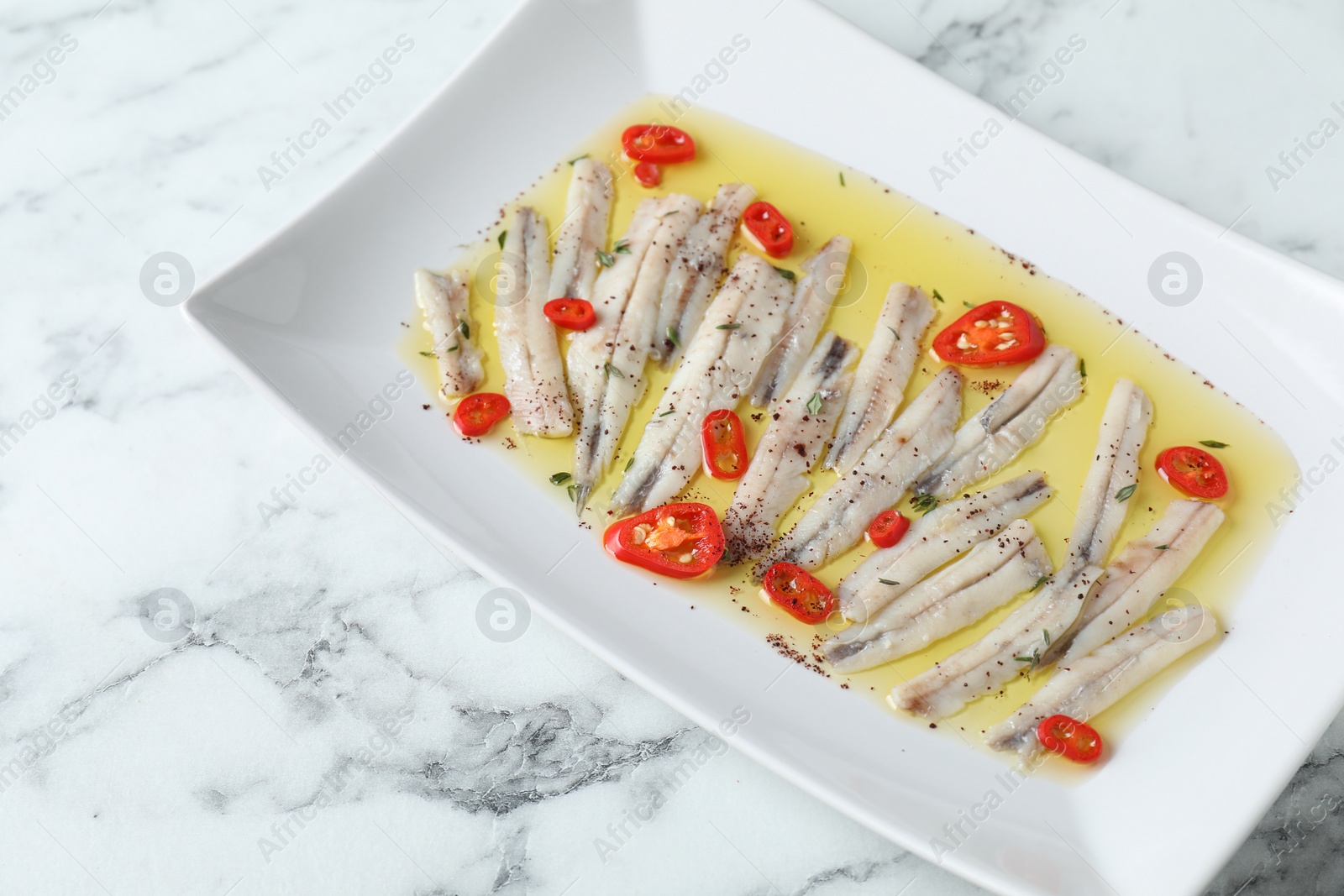 Photo of Tasty pickled anchovies with spices on white marble table