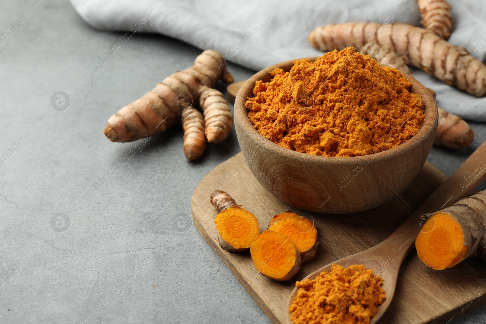 Photo of Aromatic turmeric powder and cut roots on grey table. Space for text