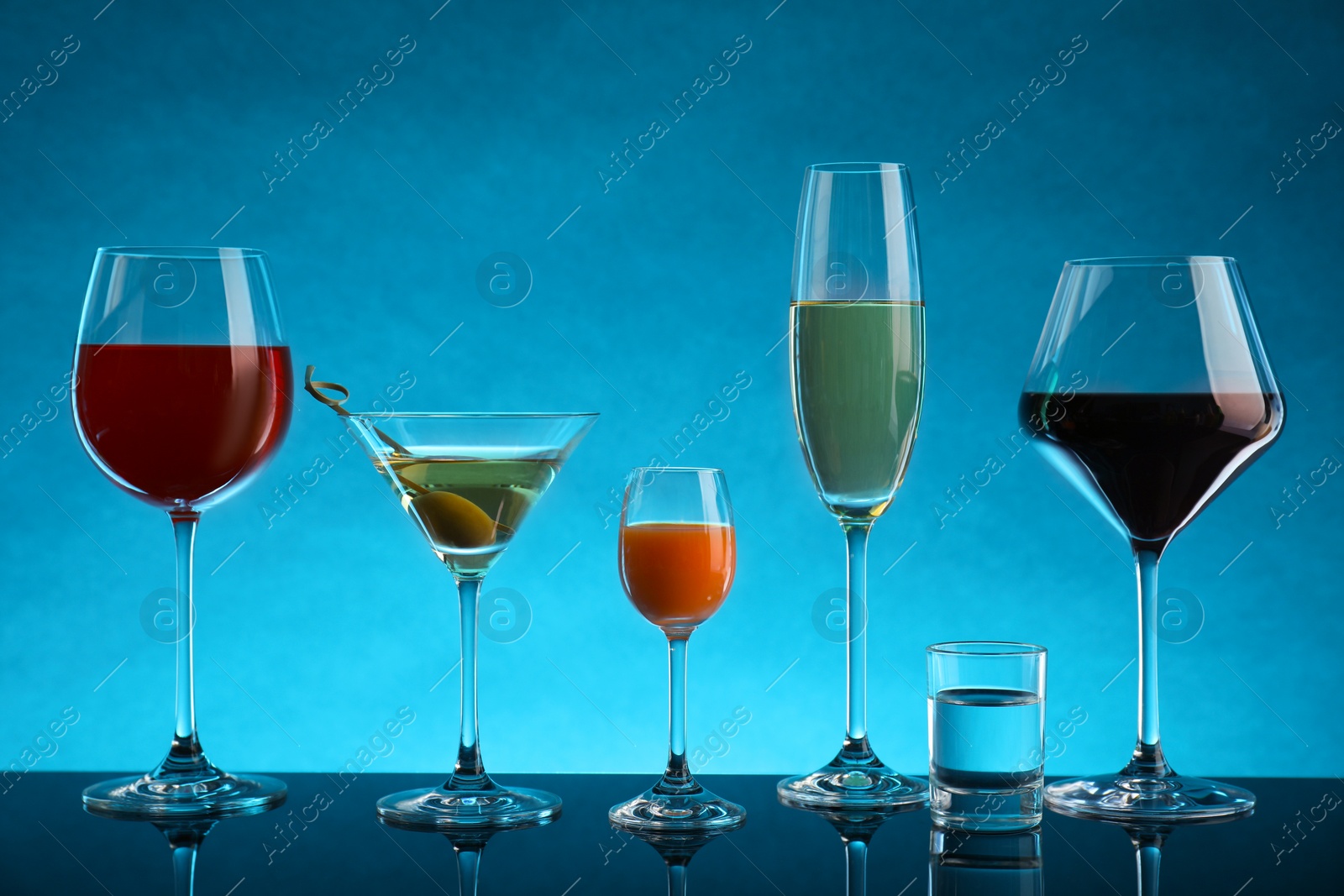 Photo of Glasses with different alcoholic drinks on table against light blue background