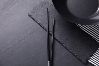 Empty iron wok and chopsticks on black table, top view. Space for text