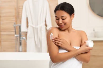 Photo of Young woman applying body cream onto arm in bathroom. Space for text