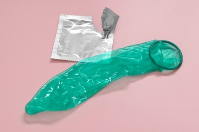 Photo of Unrolled condom and torn package on pink background. Safe sex