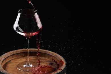 Photo of Pouring red wine into glass on wooden barrel against black background. Space for text