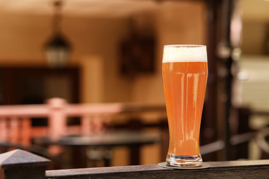 Photo of Glass of tasty beer on railing outdoors, space for text