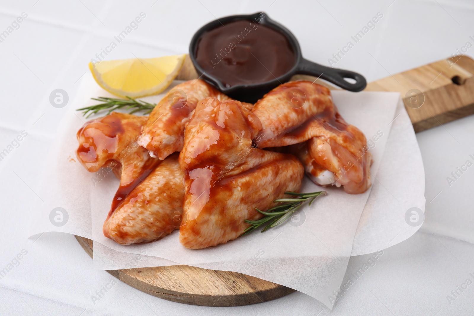 Photo of Raw chicken wings, rosemary, lemon and marinade on light tiled table, closeup