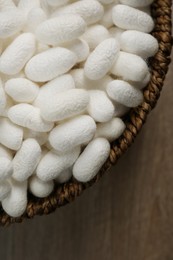 Photo of White silk cocoons in bowl on wooden table, closeup