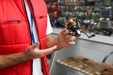 Salesman with spinning reel in sports shop, closeup. Fishing equipment