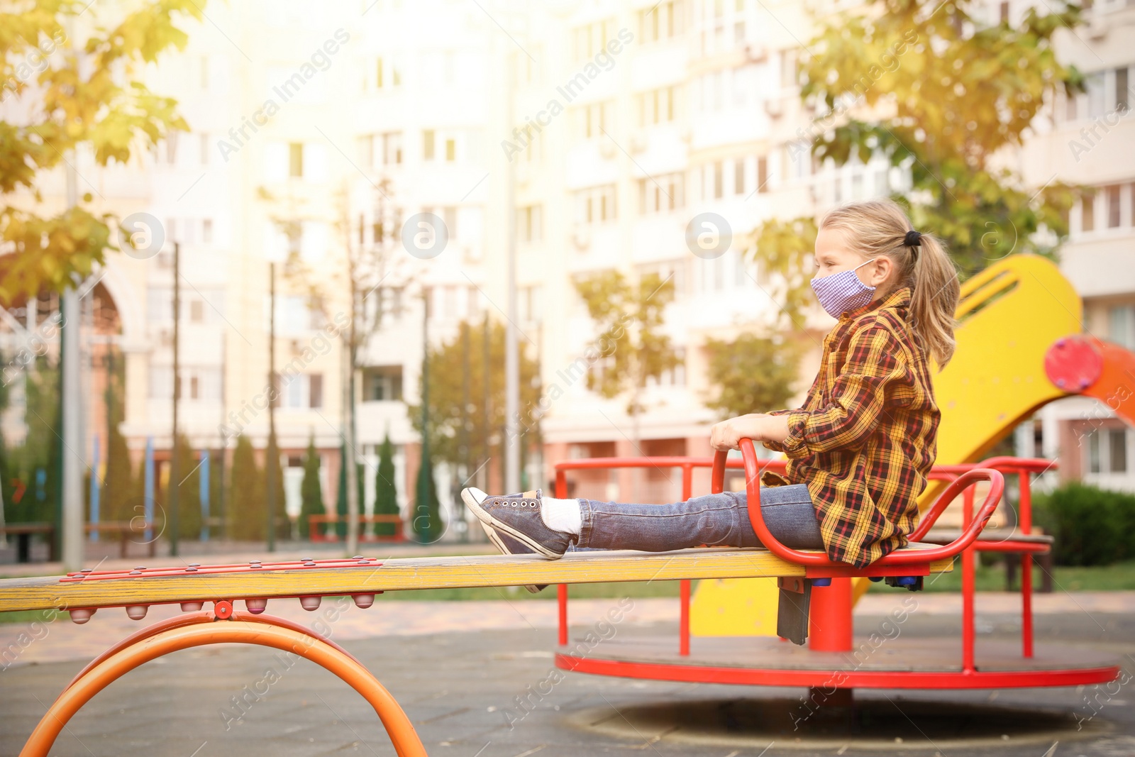 Photo of Little girl with medical face mask on playground during covid-19 quarantine