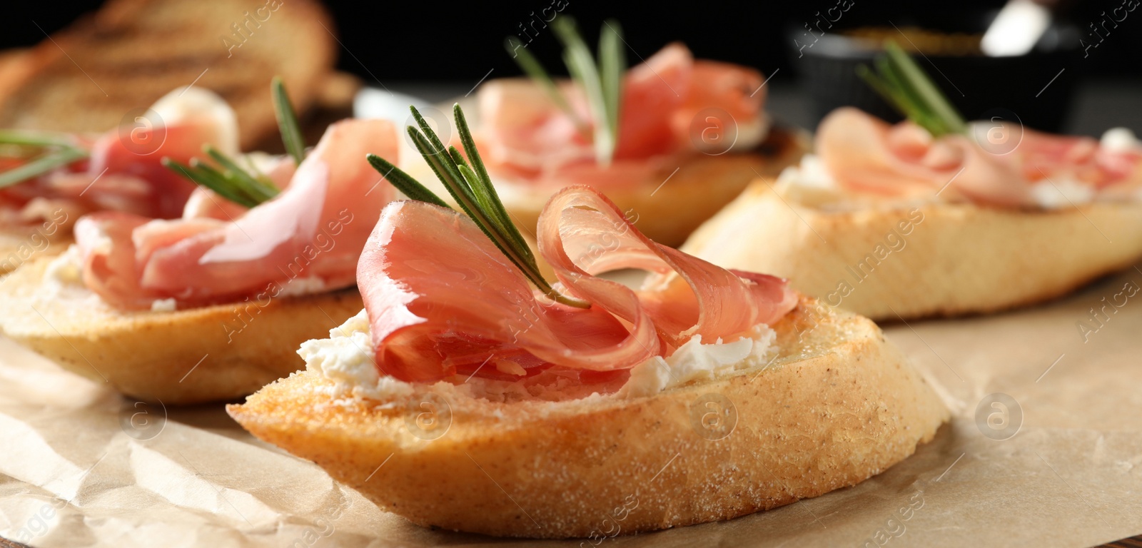 Image of Tasty bruschettas with prosciutto and cream cheese served on table, closeup. Banner design