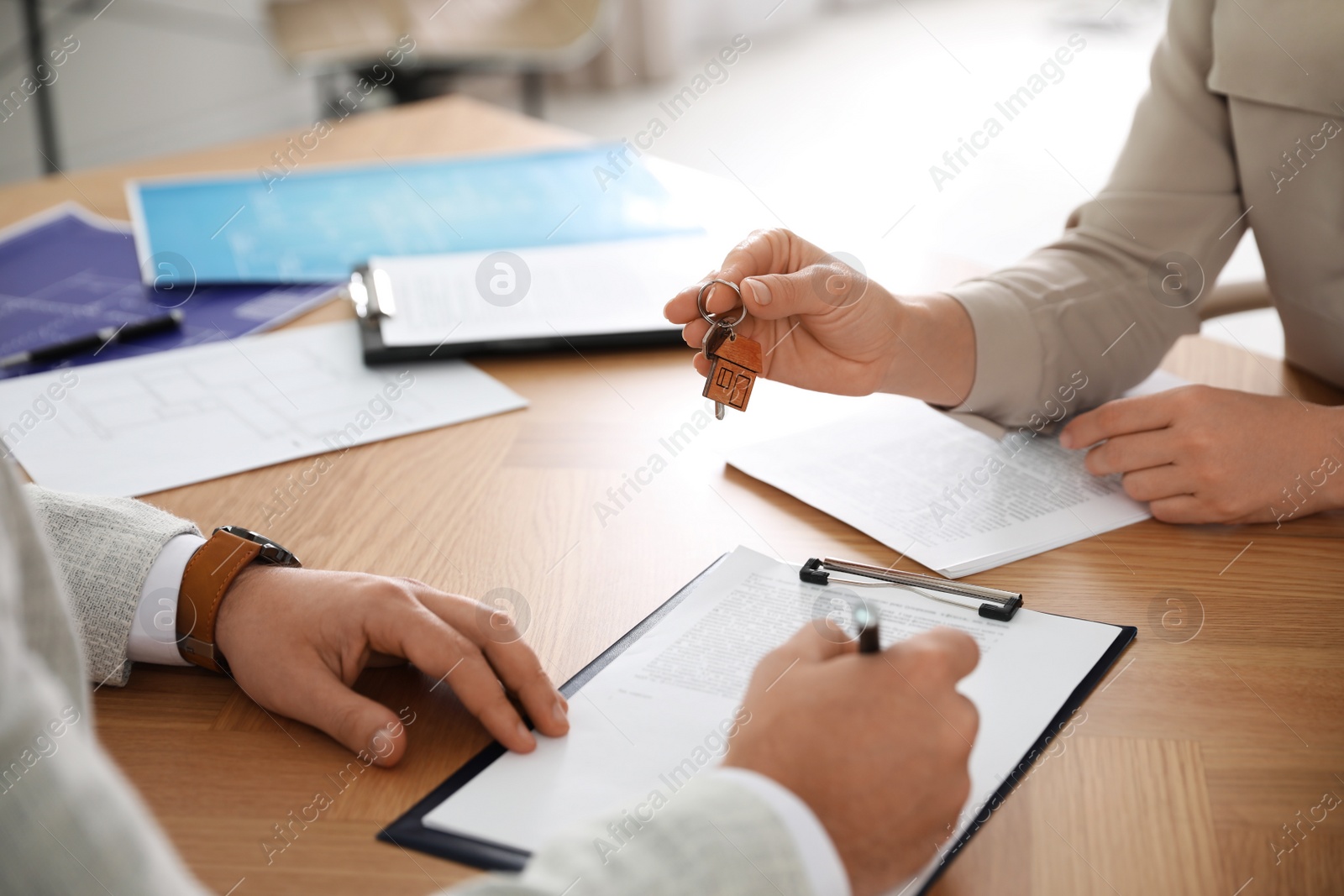 Photo of Real estate agent giving key with trinket to client in office, closeup