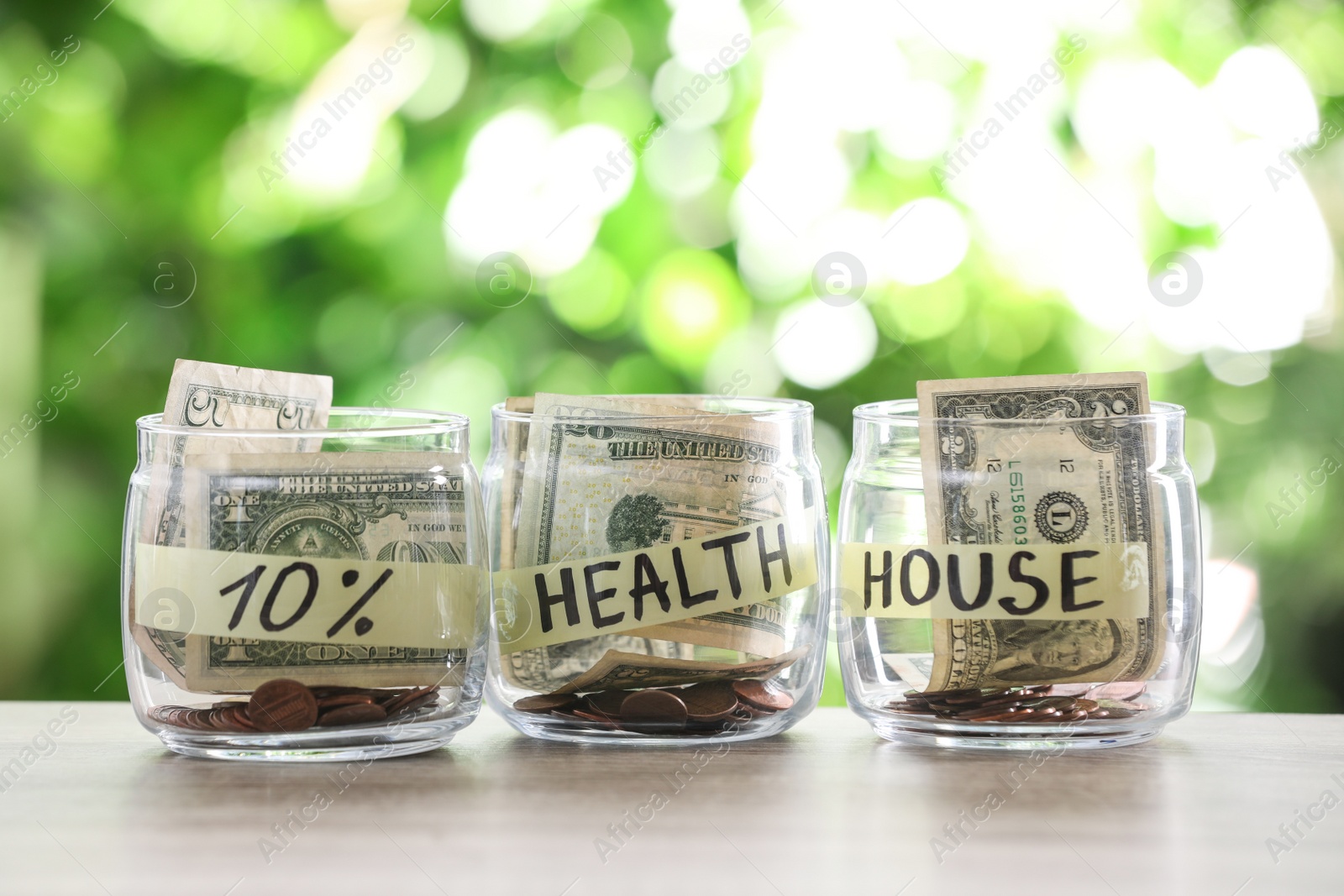 Photo of Glass jars with money for different needs on table against blurred background