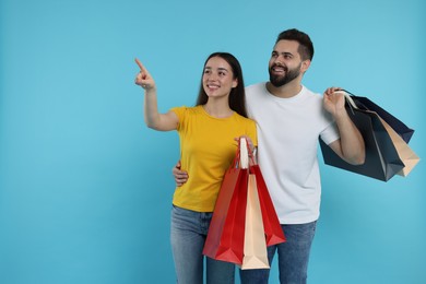 Photo of Happy couple with shopping bags looking at something on light blue background. Space for text