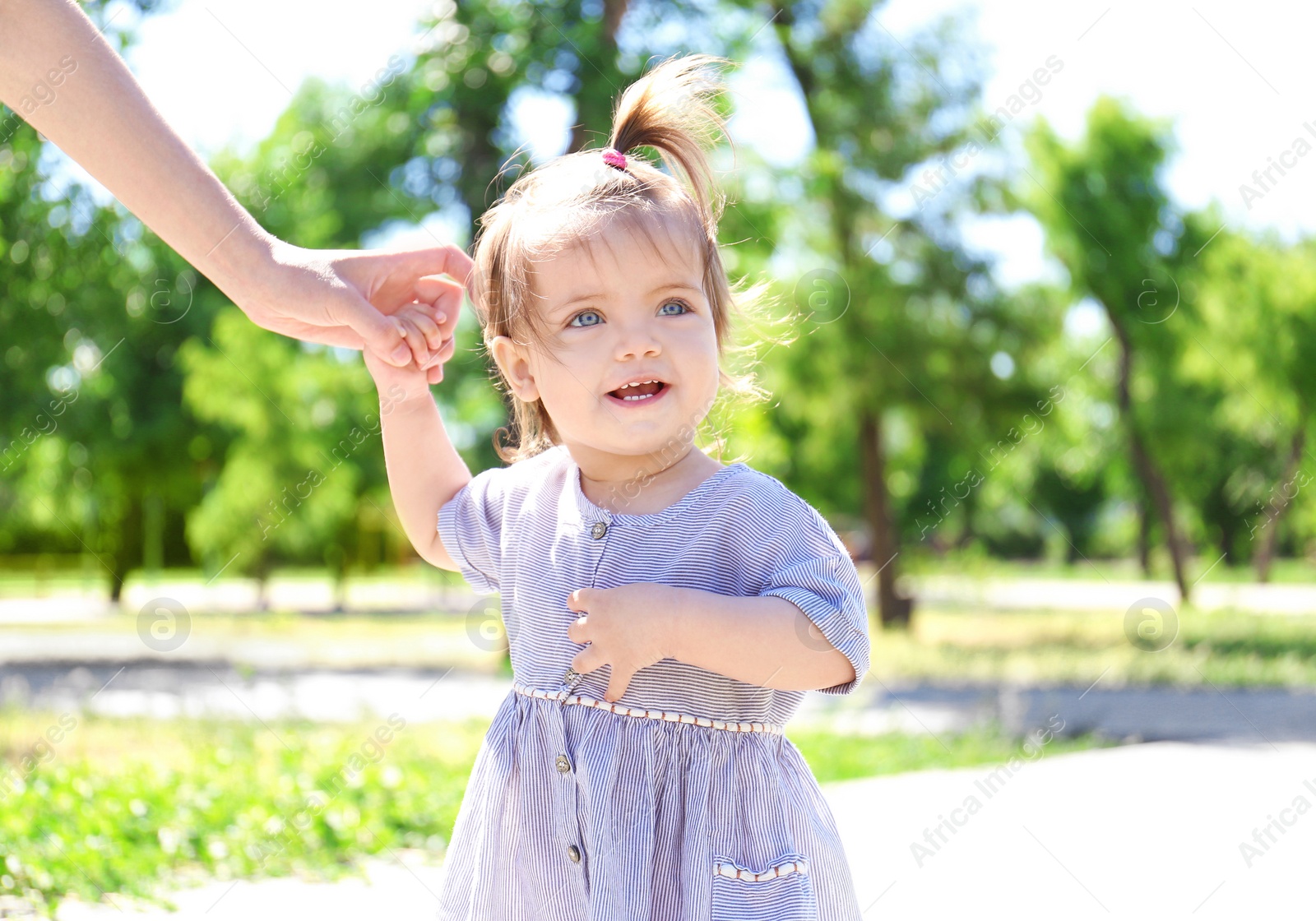 Photo of Adorable baby girl holding mother's hand while learning to walk outdoors