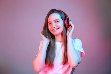 Portrait of beautiful woman with headphones in neon lights on color background