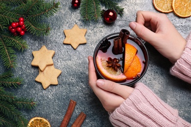 Woman with cup of aromatic mulled wine at grey table, closeup