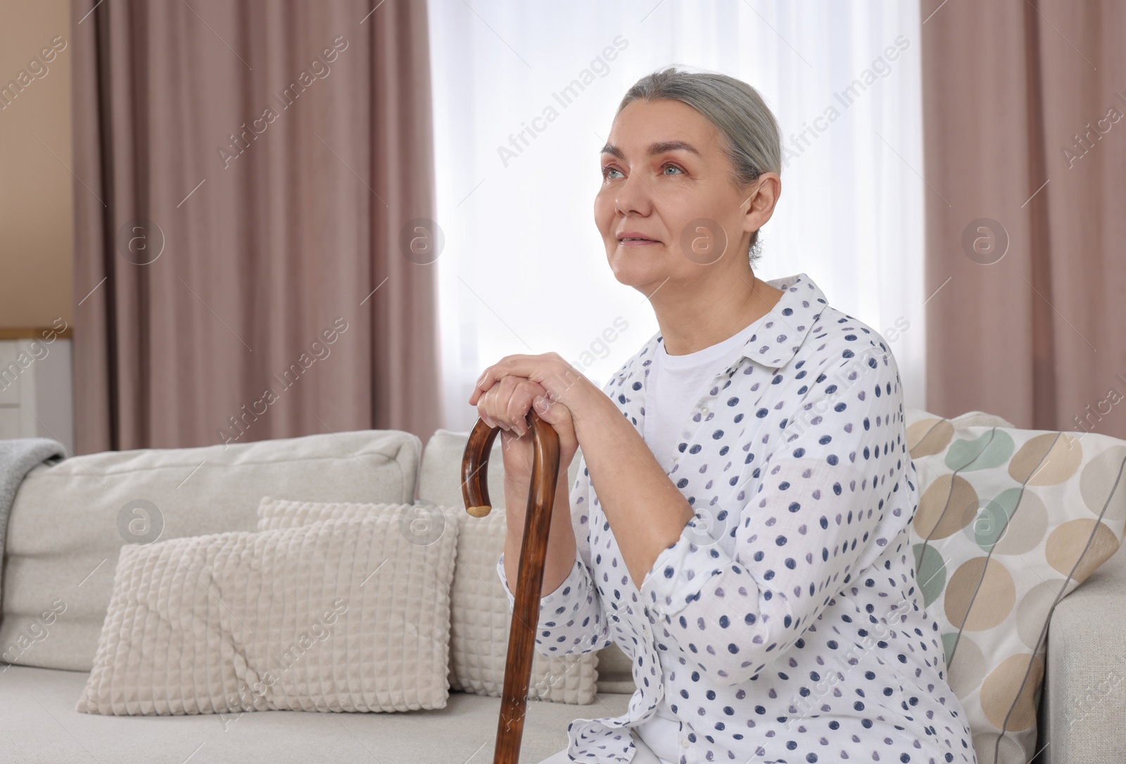 Photo of Senior woman with walking cane sitting on sofa at home. Space for text