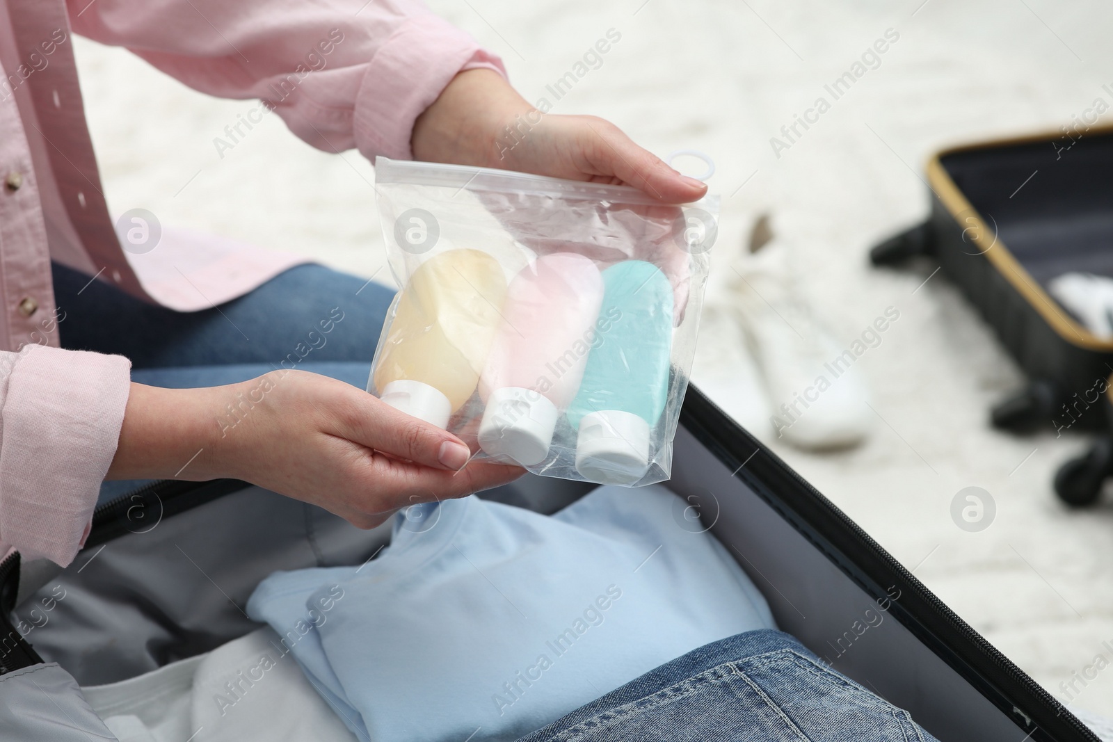 Photo of Woman holding plastic bag of cosmetic travel kit over suitcase, closeup and space for text. Bath accessories