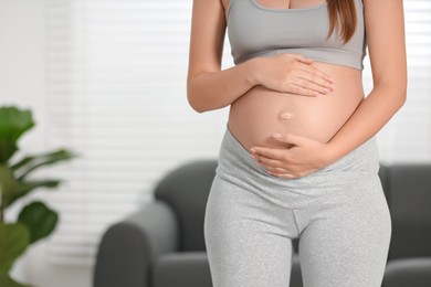 Pregnant woman standing near sofa at home, closeup. Space for text