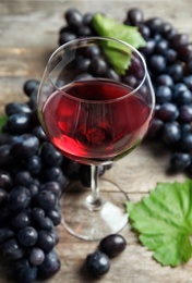 Photo of Glass of red wine and fresh ripe juicy grapes on table