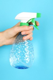 Woman holding plastic spray bottle on light blue background, closeup