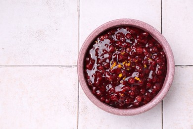 Tasty cranberry sauce in bowl on white tiled table, top view. Space for text