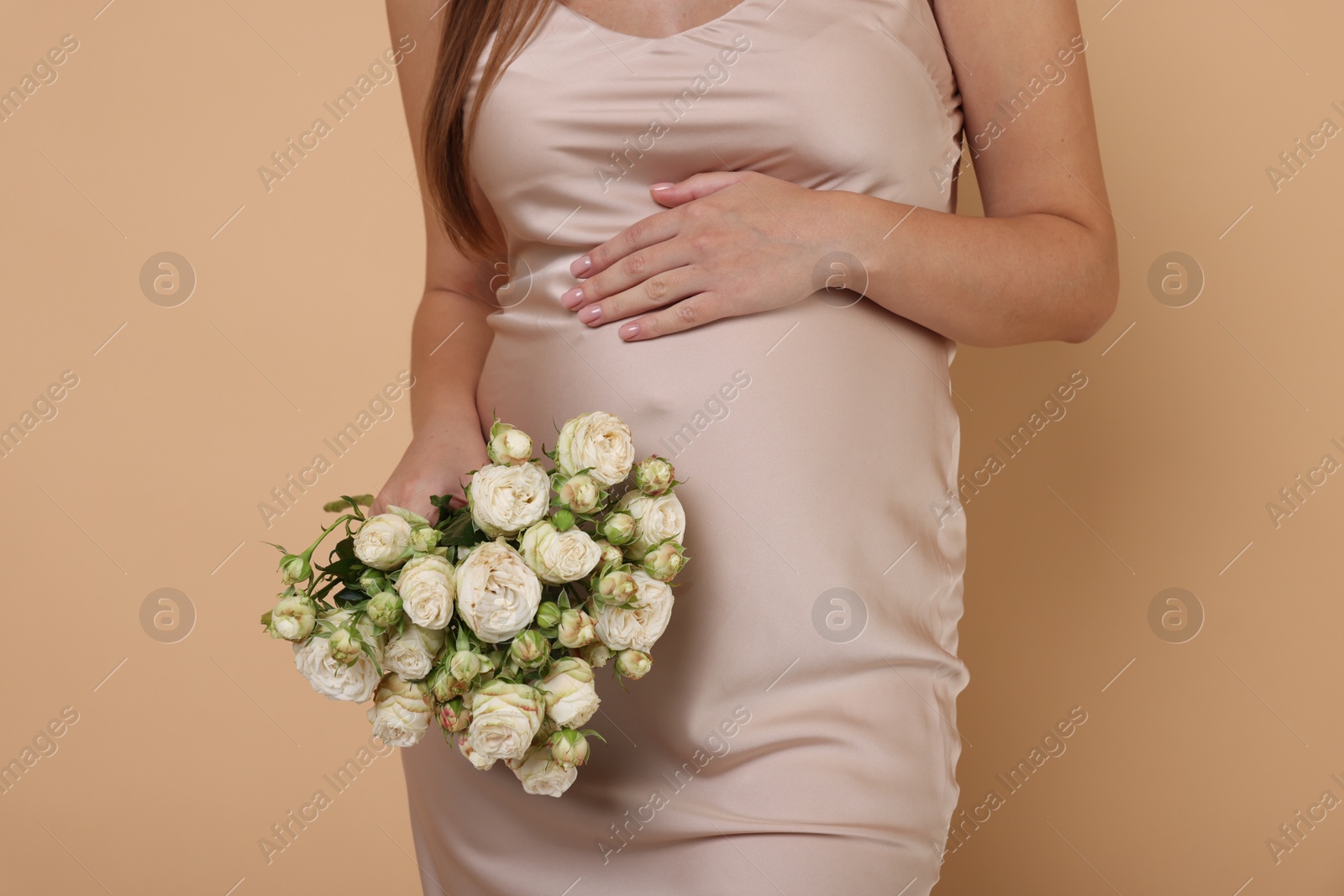 Photo of Pregnant woman in dress with bouquet of roses on beige background, closeup