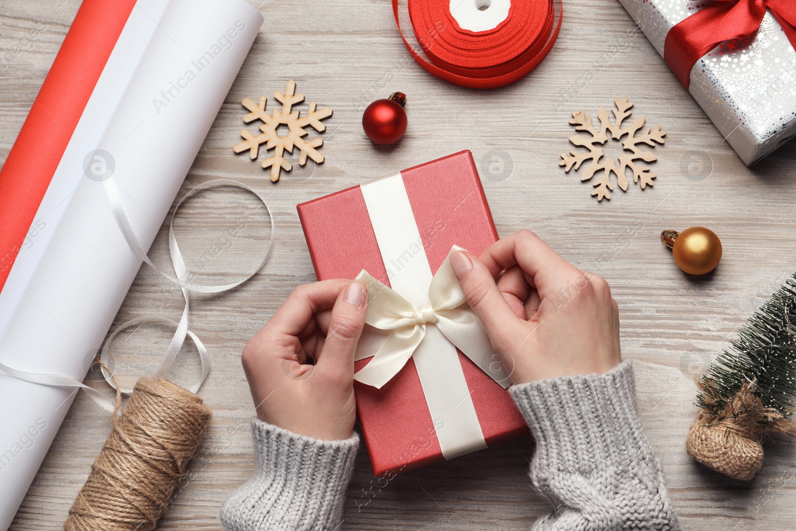 Photo of Christmas present. Woman tying ribbon bow on gift box at white wooden table, top view